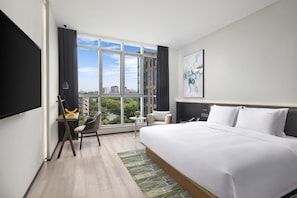 A modern hotel room with a large bed, a desk with a chair, a small table, and a view of the city through large windows. - Holiday Inn TongXiang by IHG (Jiaxing)