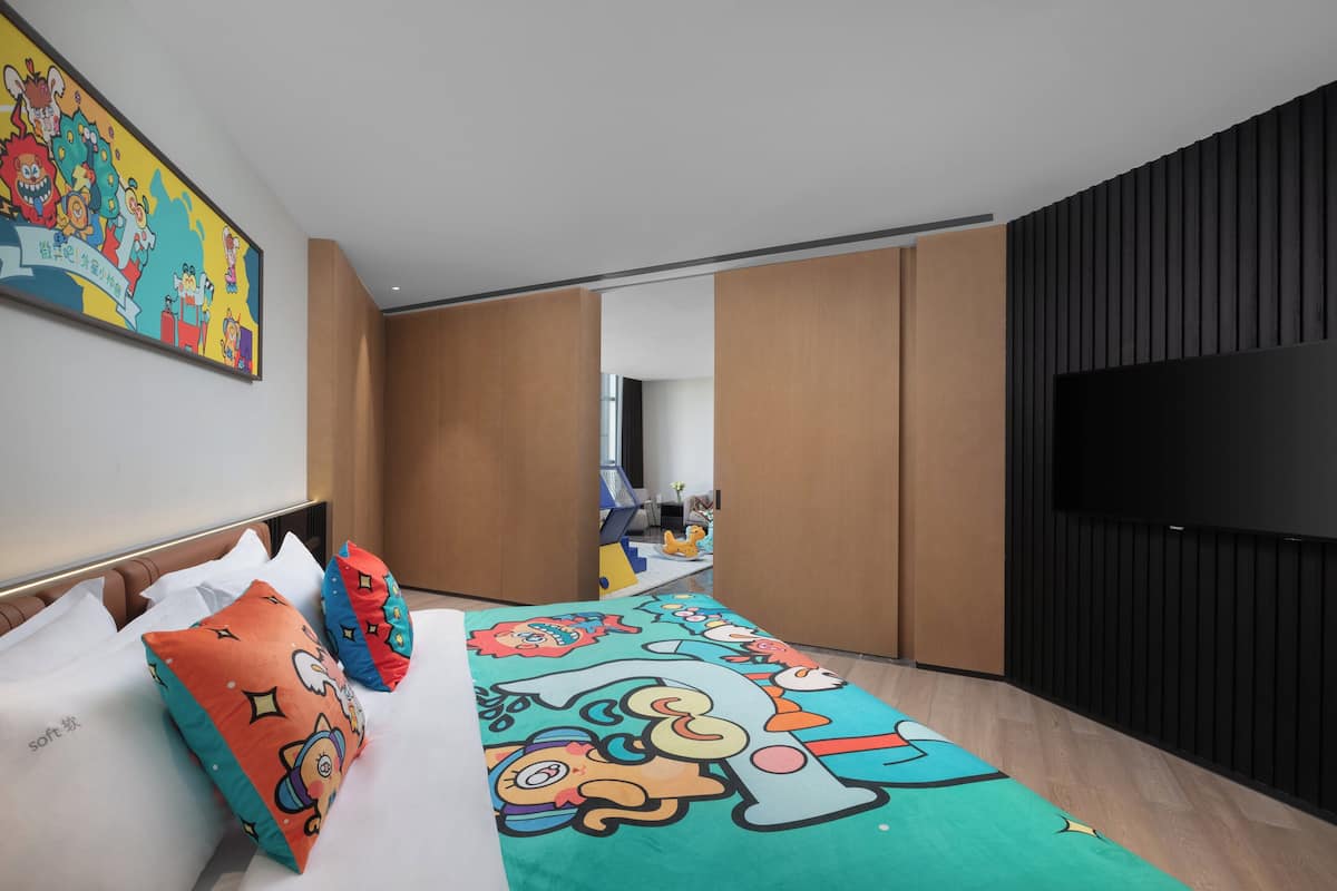 Una habitación de hotel moderna con una cama grande, almohadas coloridas, un televisor de pantalla plana y un ventanal amplio.