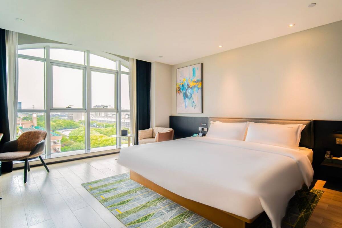 Habitación de hotel moderna con una cama grande, un escritorio y una silla. Cuenta con un amplio ventanal con vistas a la ciudad.