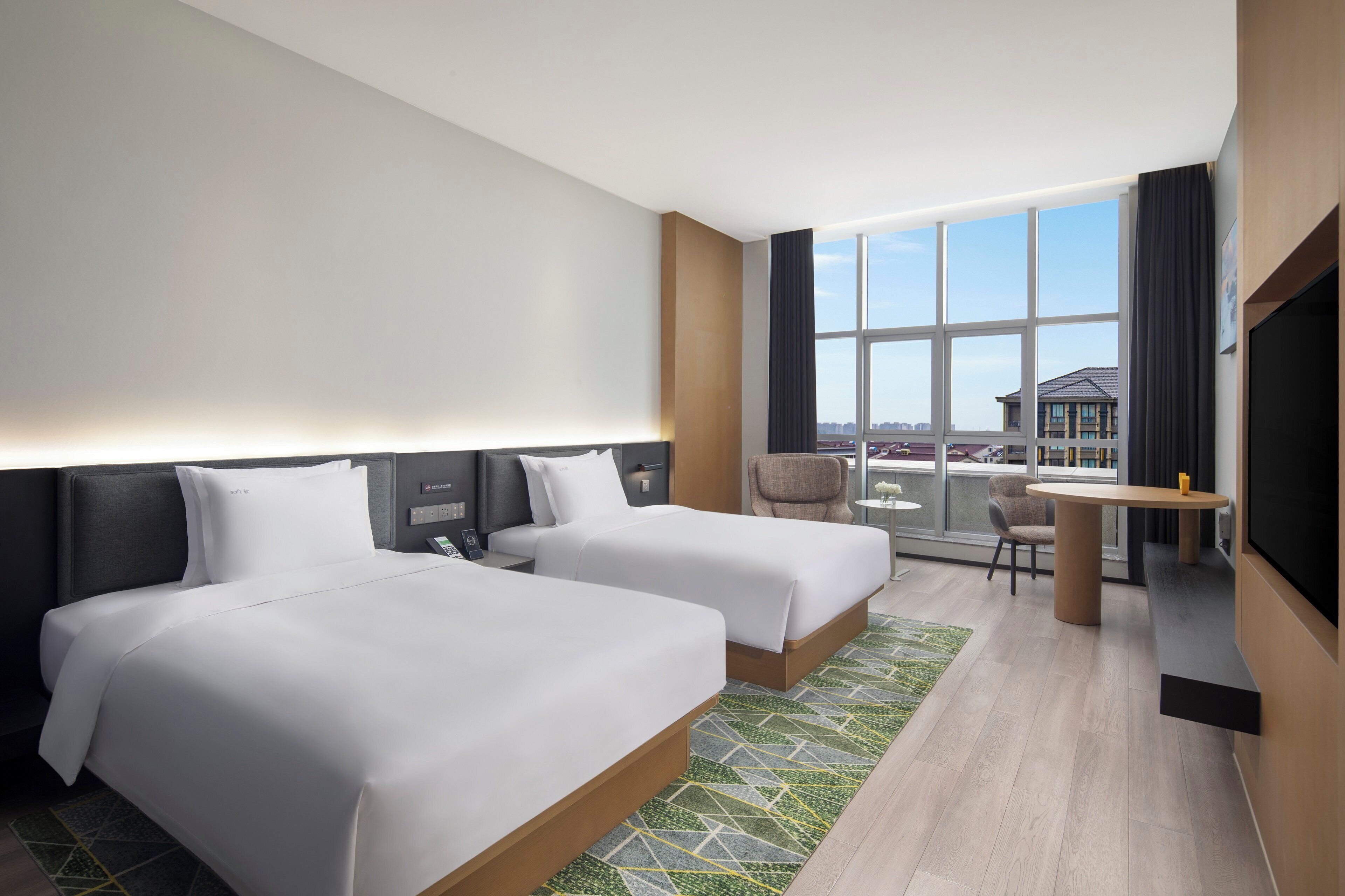 A hotel room with two beds, a small table, a chair, and a TV.