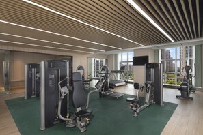 Une salle de sport moderne équipée de divers appareils d’exercice, dotée de grandes fenêtres et offrant une vue sur les immeubles de grande hauteur.
