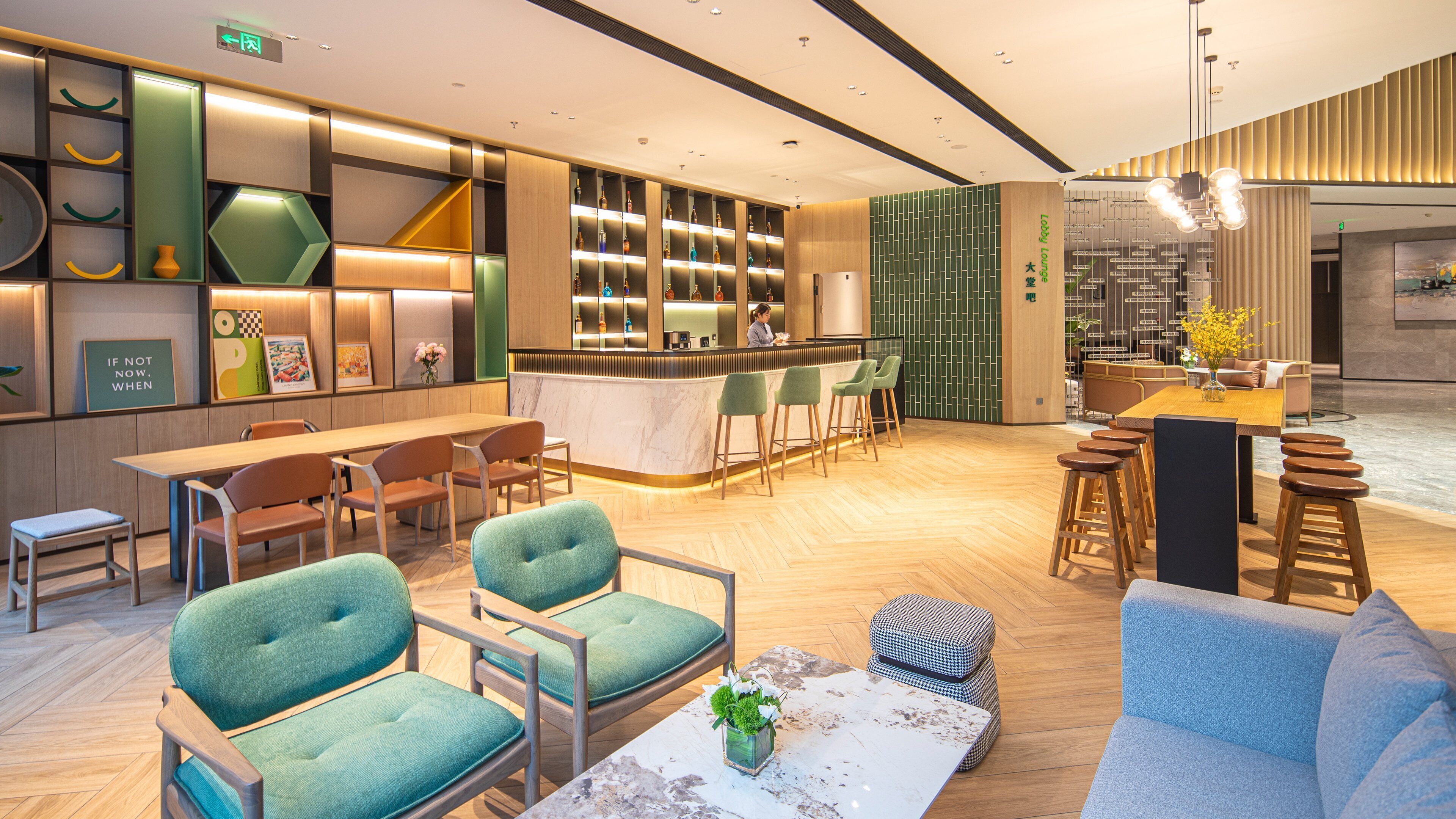 A modern lounge area with a bar, seating, and a display of bottles.