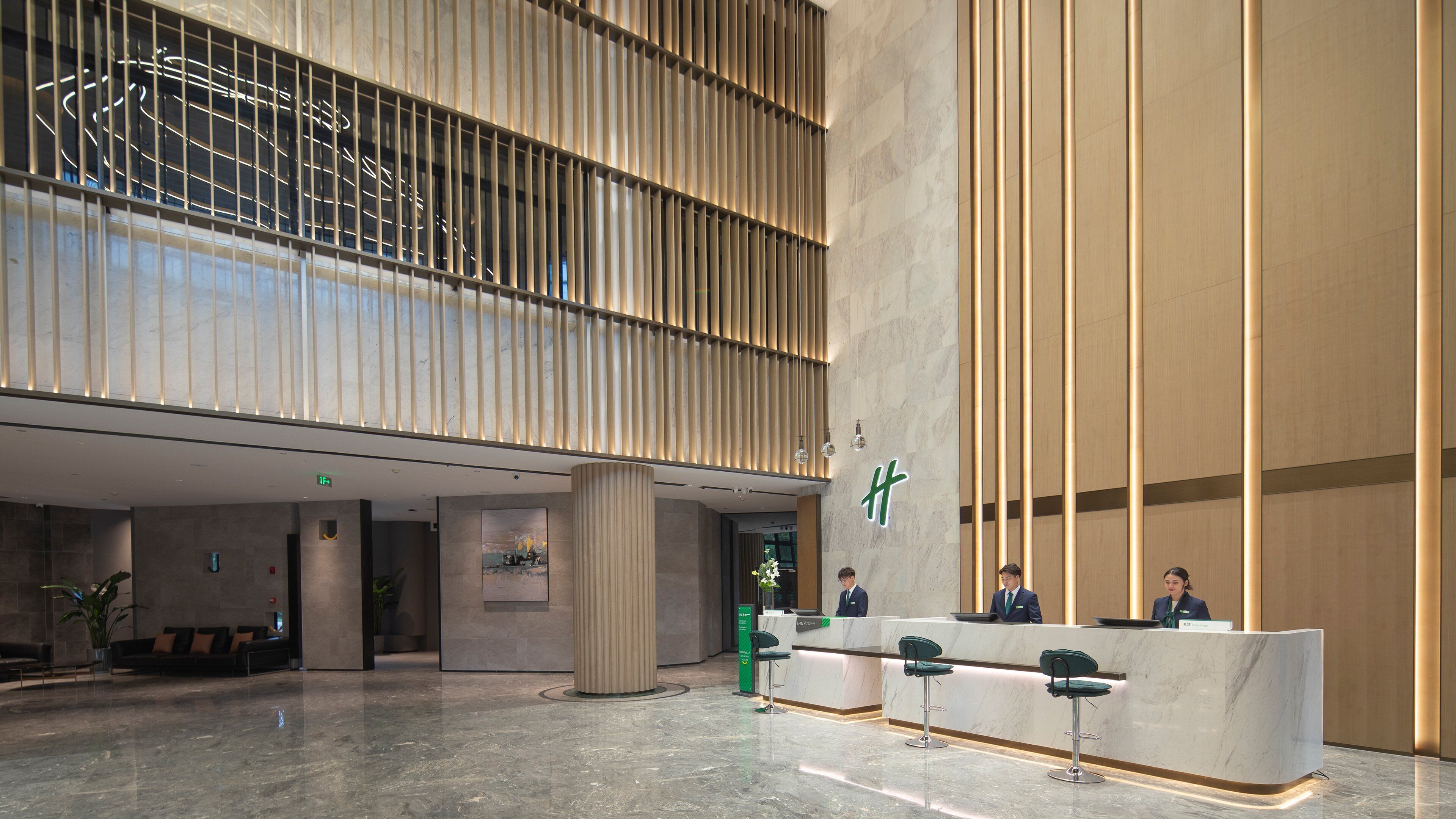 A modern hotel lobby with a reception desk, seating area, and a large glass wall.