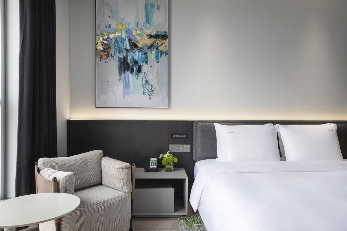 Habitación de hotel moderna con una cama, un sofá, una mesita y una mesita de noche con un teléfono y una planta.