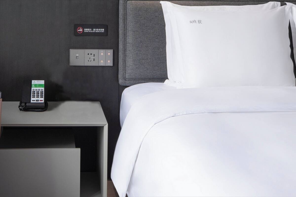 Una habitación de hotel con cama, mesita de noche y un panel de control en la pared.