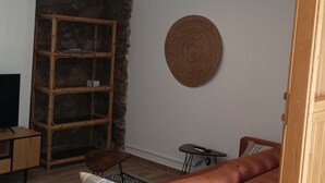 Un salon comprenant un téléviseur, un meuble en bois, une décoration murale ronde en fibres tressées et un canapé en cuir marron.
