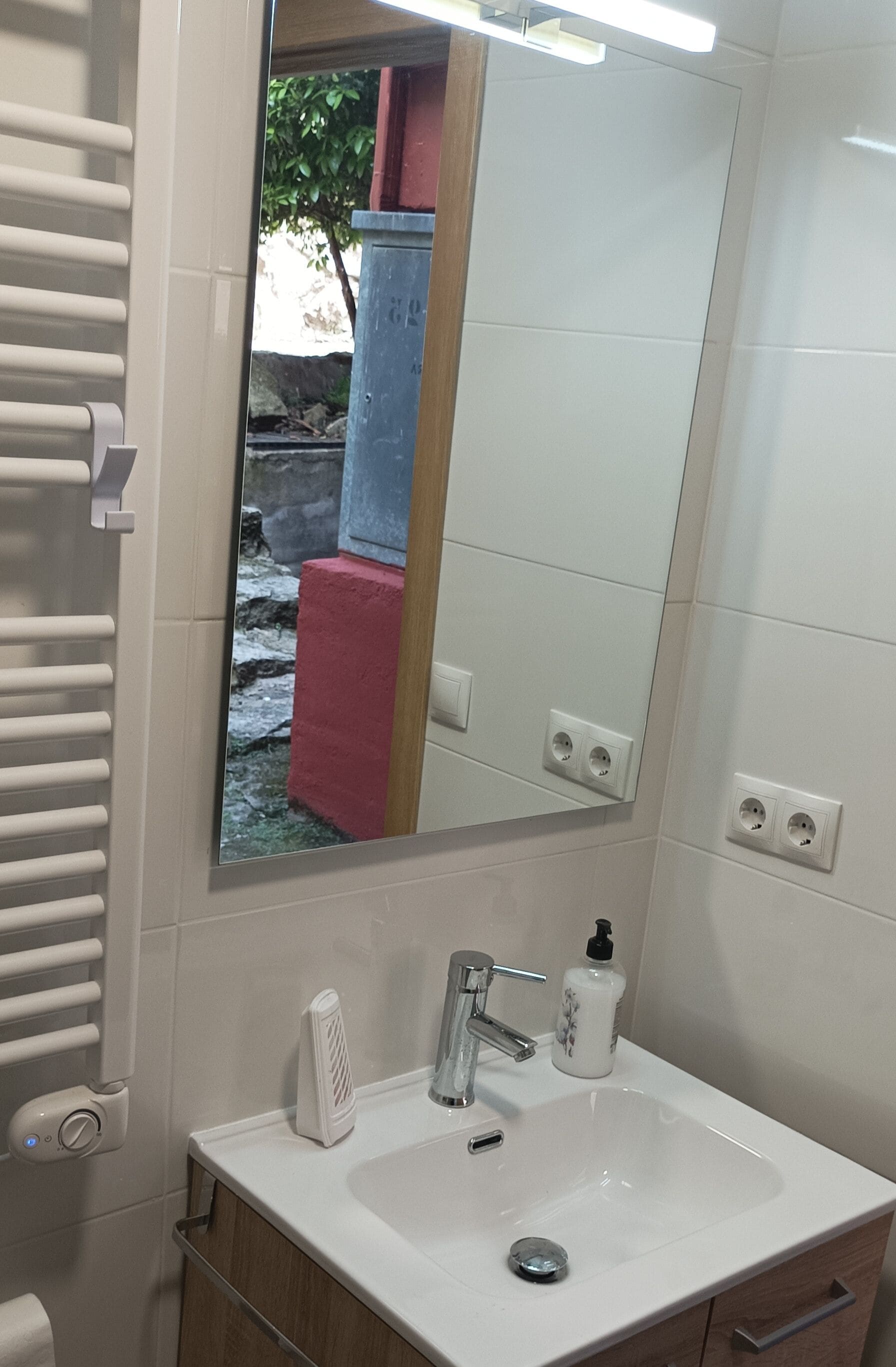 Une salle de bain avec un lavabo blanc, un miroir, un porte-serviettes et un radiateur.