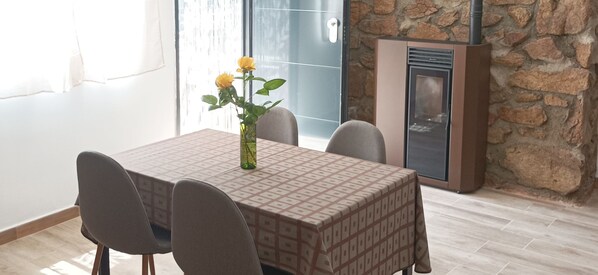 Un comedor con una mesa dispuesta para cuatro personas, un jarrón con flores amarillas y una pared de piedra con chimenea.