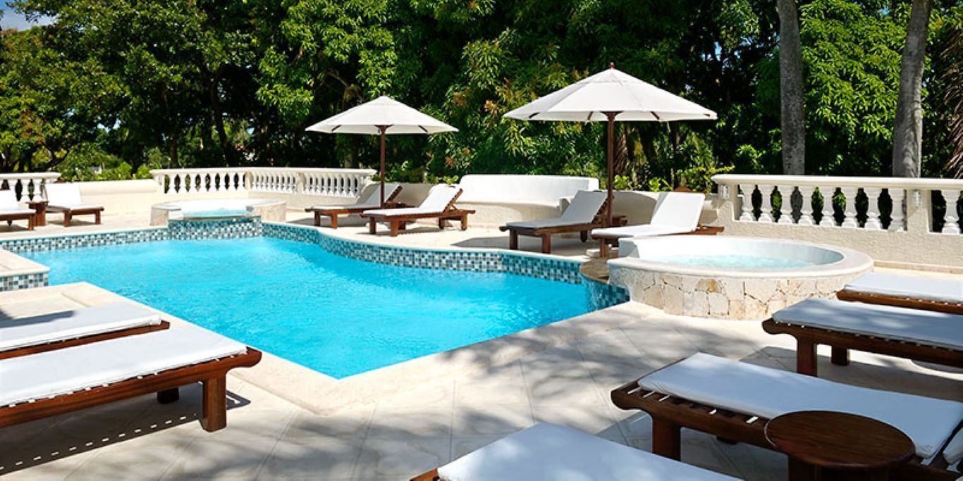 Un área junto a la piscina con sillones de descanso, sombrillas y un jacuzzi.