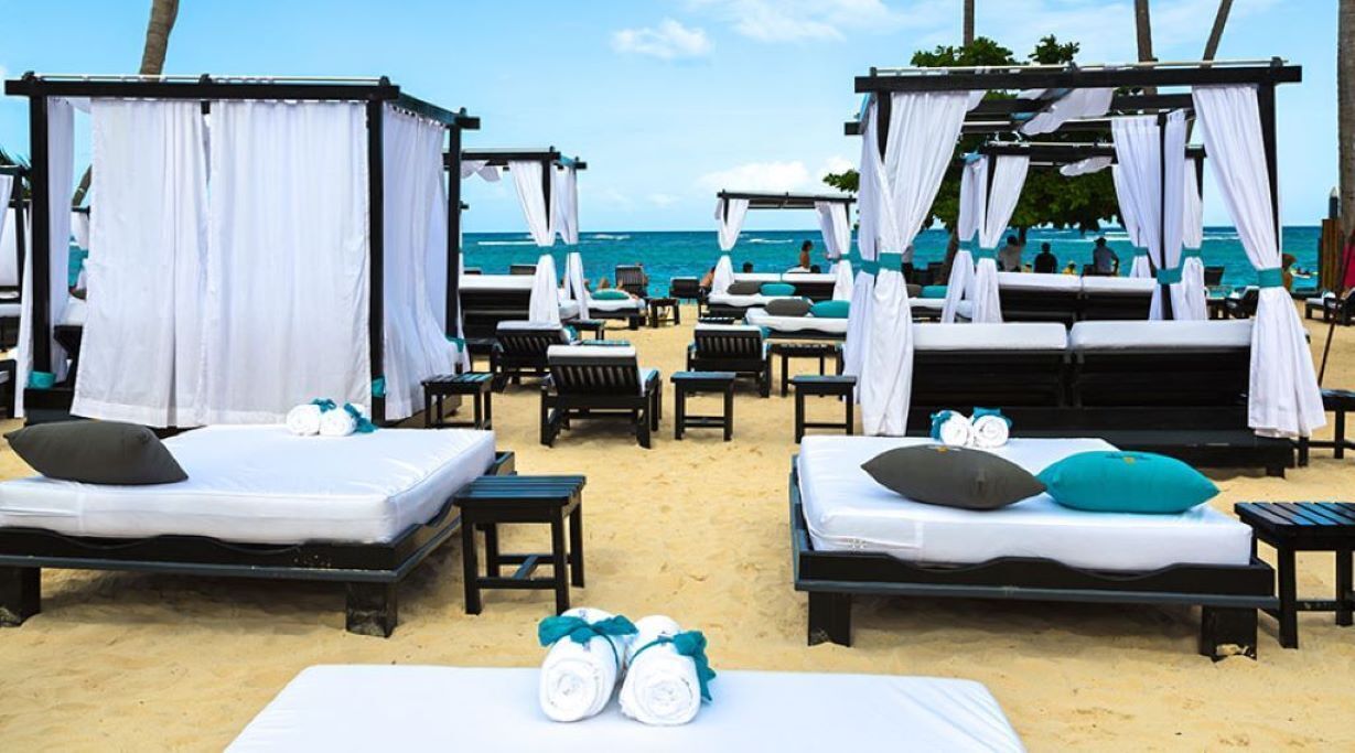 Ein Hotel am Strand mit Baldachinbetten, Liegestühlen und Blick auf den Ozean.