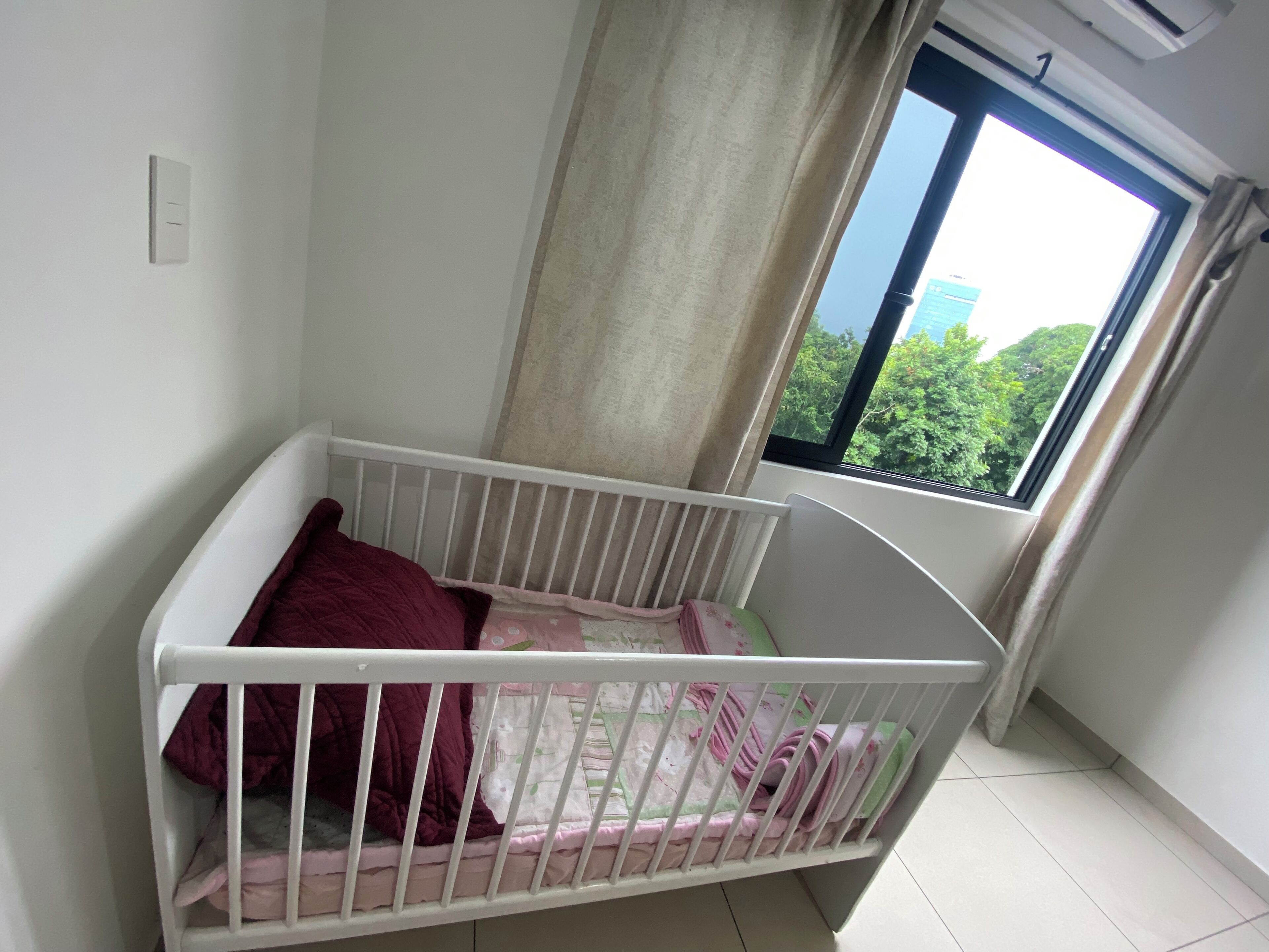 A white crib with a red blanket and a floral bedspread.