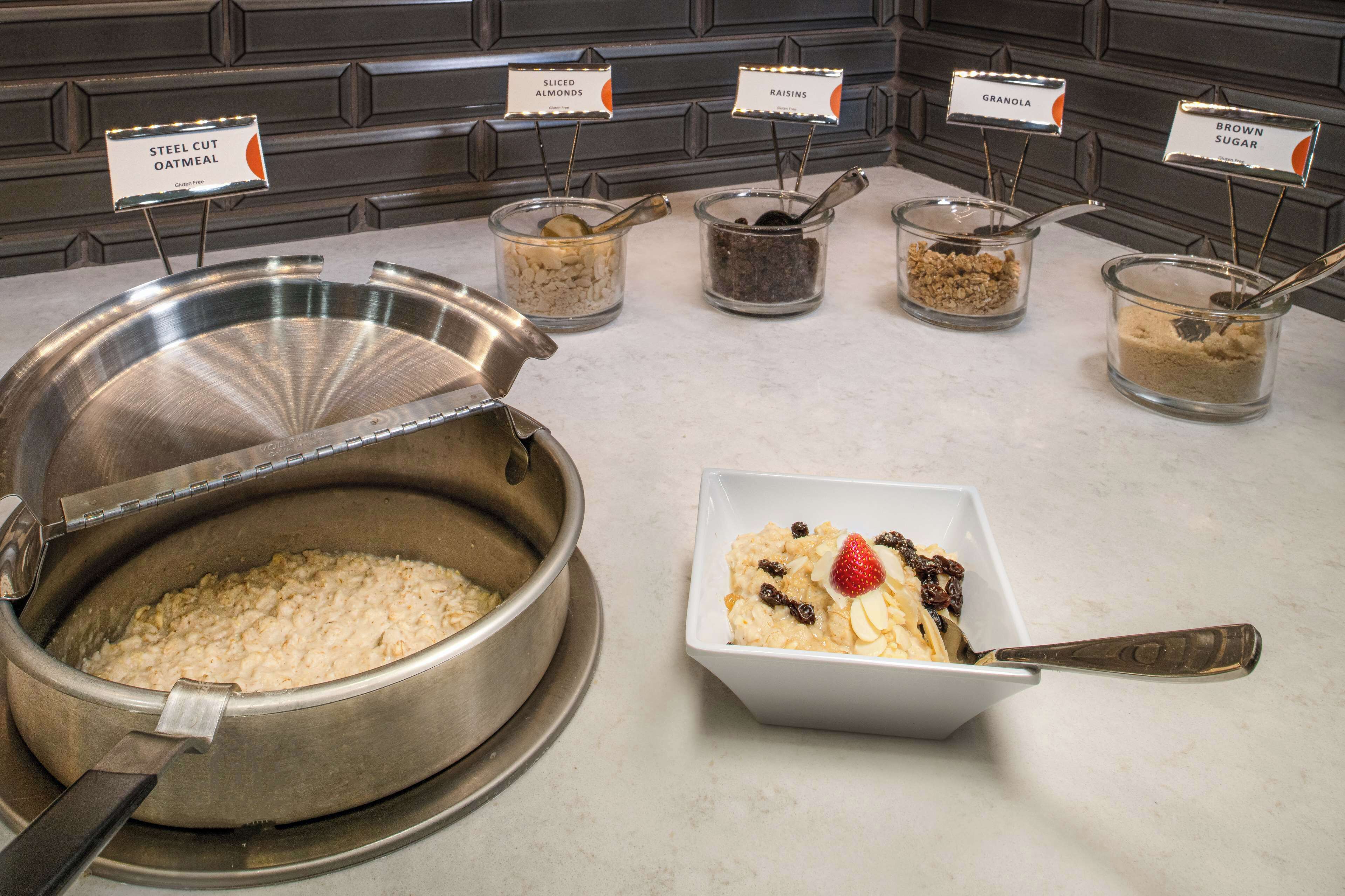 Buffet com diversas opções de comida, incluindo aveia em pedaços, amêndoas laminadas, passas, granola e açúcar mascavo.