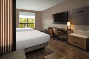 Una habitación de hotel moderna con una cama grande, un escritorio, una silla y un televisor fijado a la pared.