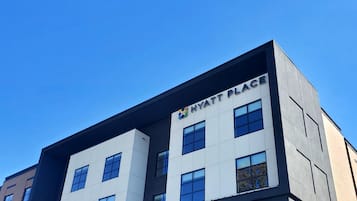 A modern building with a 'Hyatt Place' sign, a 'Parking' sign, and a clear blue sky.