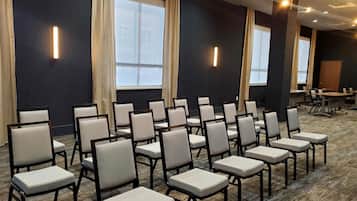 A conference room with rows of chairs, large windows, and a carpeted floor.
