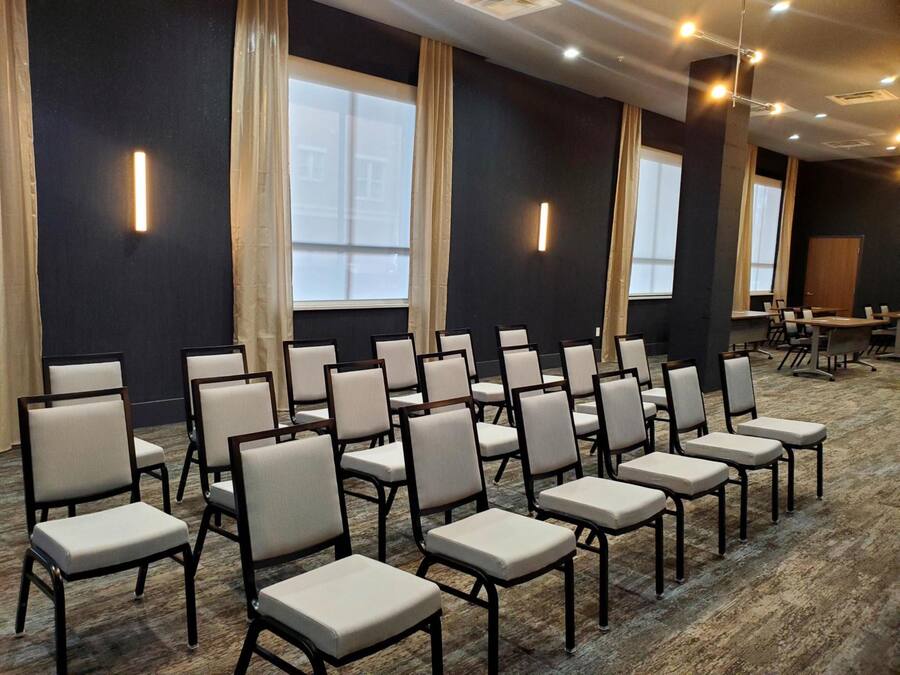 A conference room with rows of chairs, large windows, and a carpeted floor.
