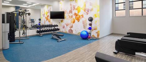 A modern gym with cardio equipment, weightlifting stations, and a blue carpeted floor.