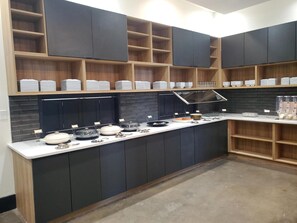 Una cocina moderna con armarios oscuros, estantes de madera y una isla central con diversos utensilios de cocina.