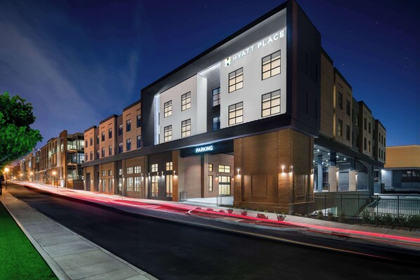 Un moderno edificio de hotel con un letrero de "HYATT PLACE", una entrada de estacionamiento y una fachada bien iluminada.