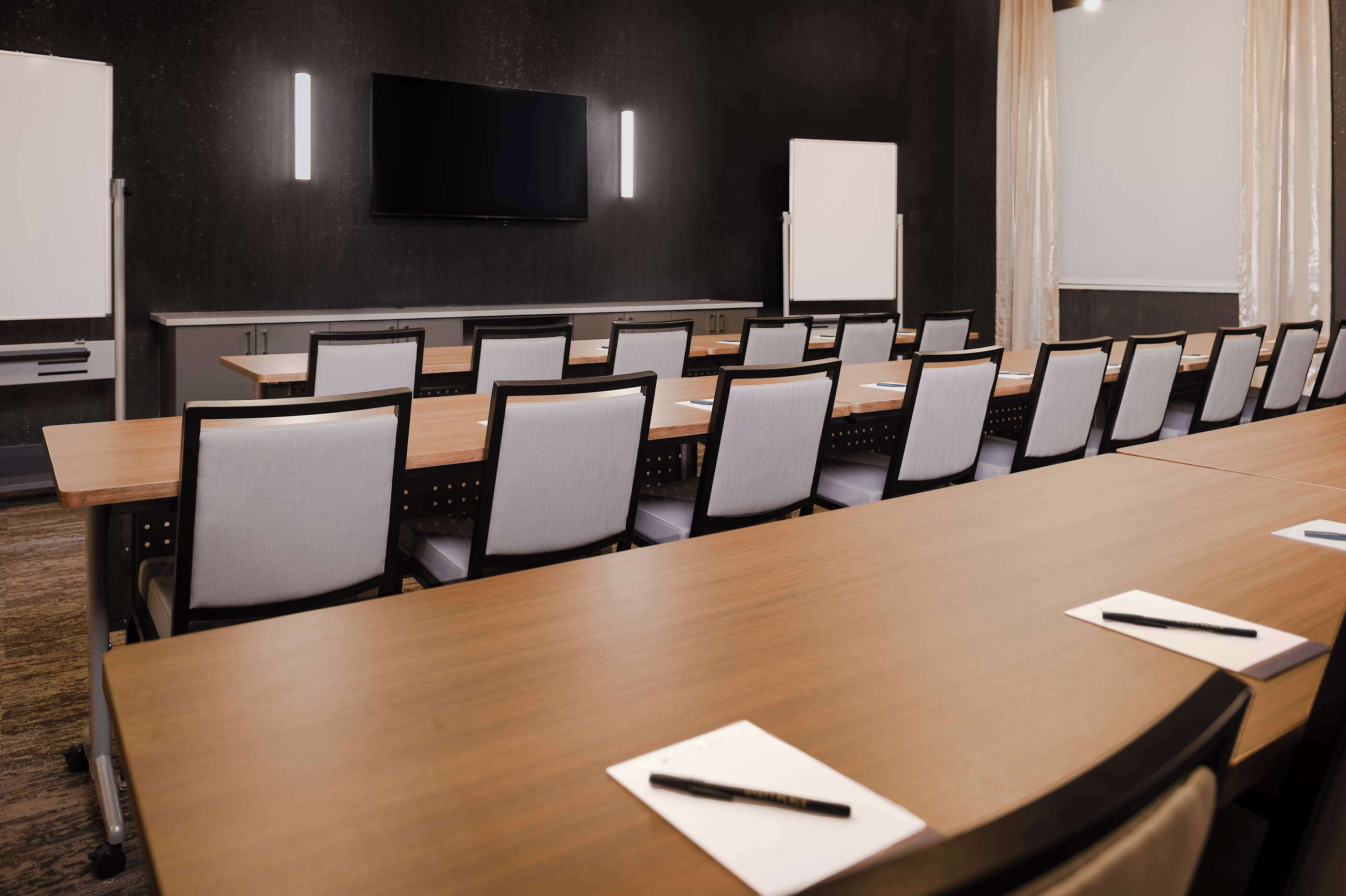 Un salón de conferencias con una larga mesa, sillas, un televisor y una pizarra.