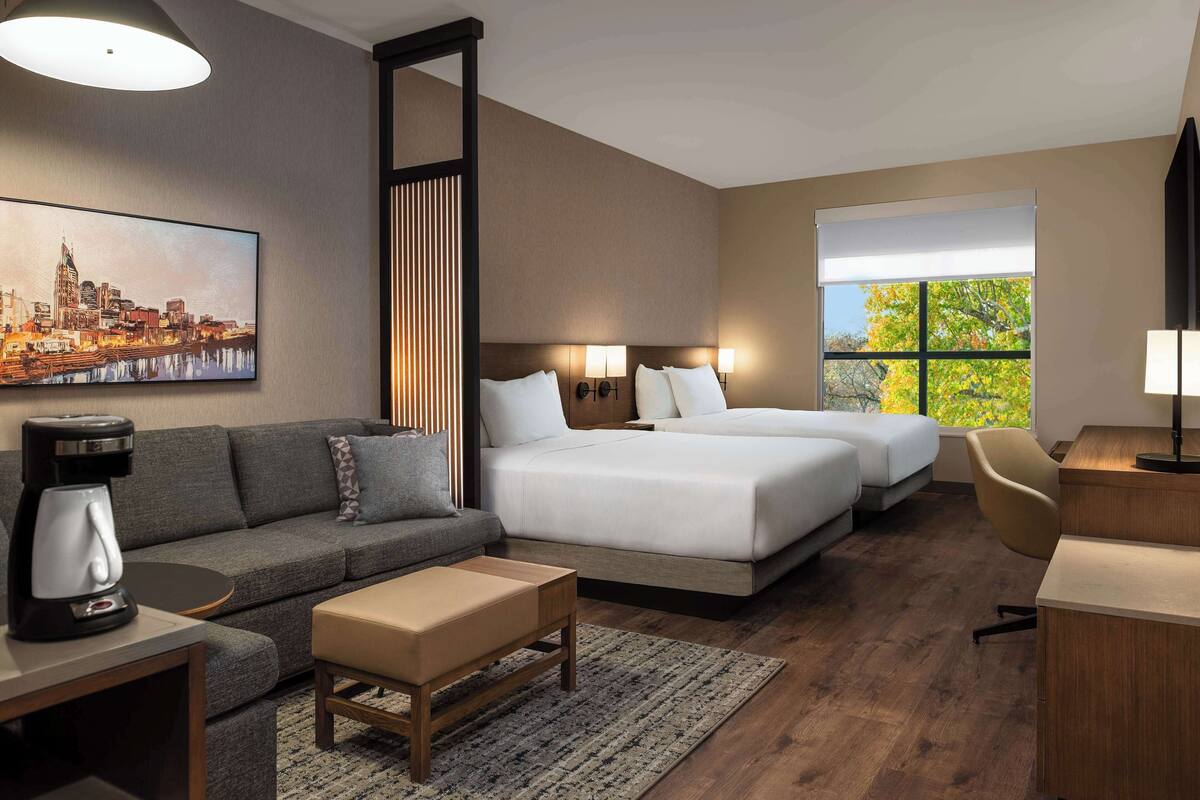 A hotel room with a sofa, two beds, a desk, and a coffee maker.