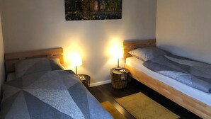 A hotel room with two beds, a small round table, a lamp, and a painting on the wall.