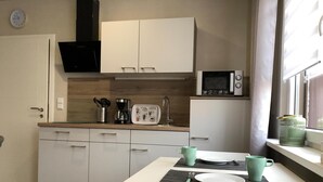 A compact kitchen with white cabinets, a microwave, a coffee maker, and a dining table with a placemat.