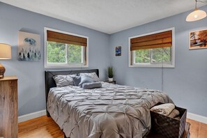 A bedroom with a bed, two windows with blinds, a nightstand, a lamp, and a wall with a picture. - Warm Chalet in Emerald Lakes, Poconos! Lakes/Pools/Deck/Kayak/Fire pits/Grill (Long Pond)