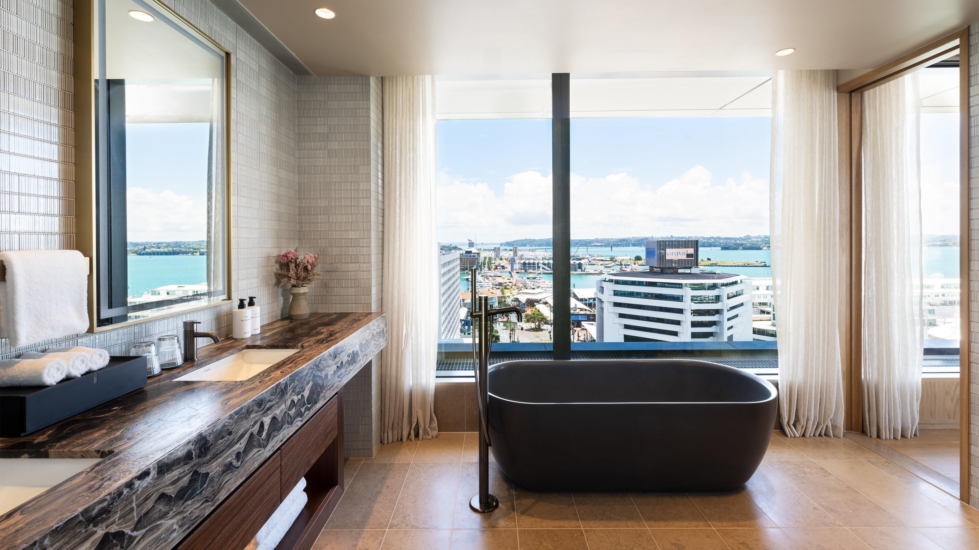 A modern bathroom with a large window, a bathtub, and a vanity with a mirror.