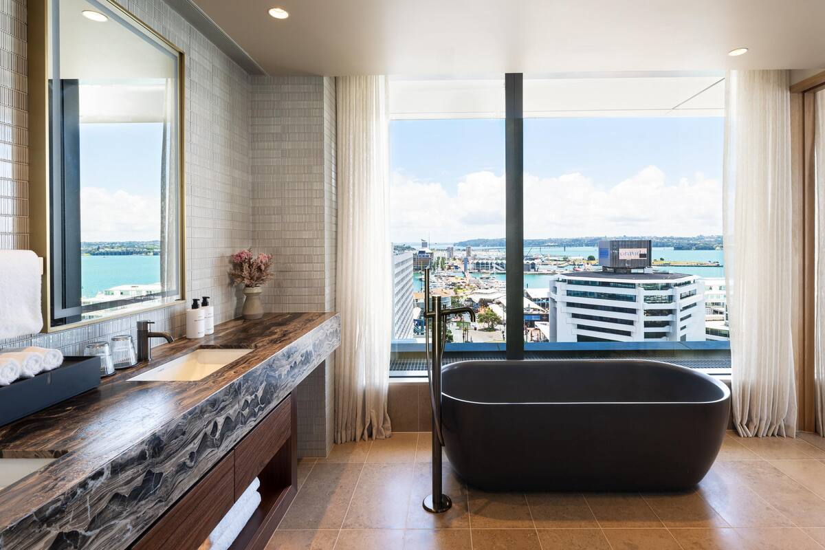 A modern bathroom with a large window, a bathtub, and a vanity with a mirror.