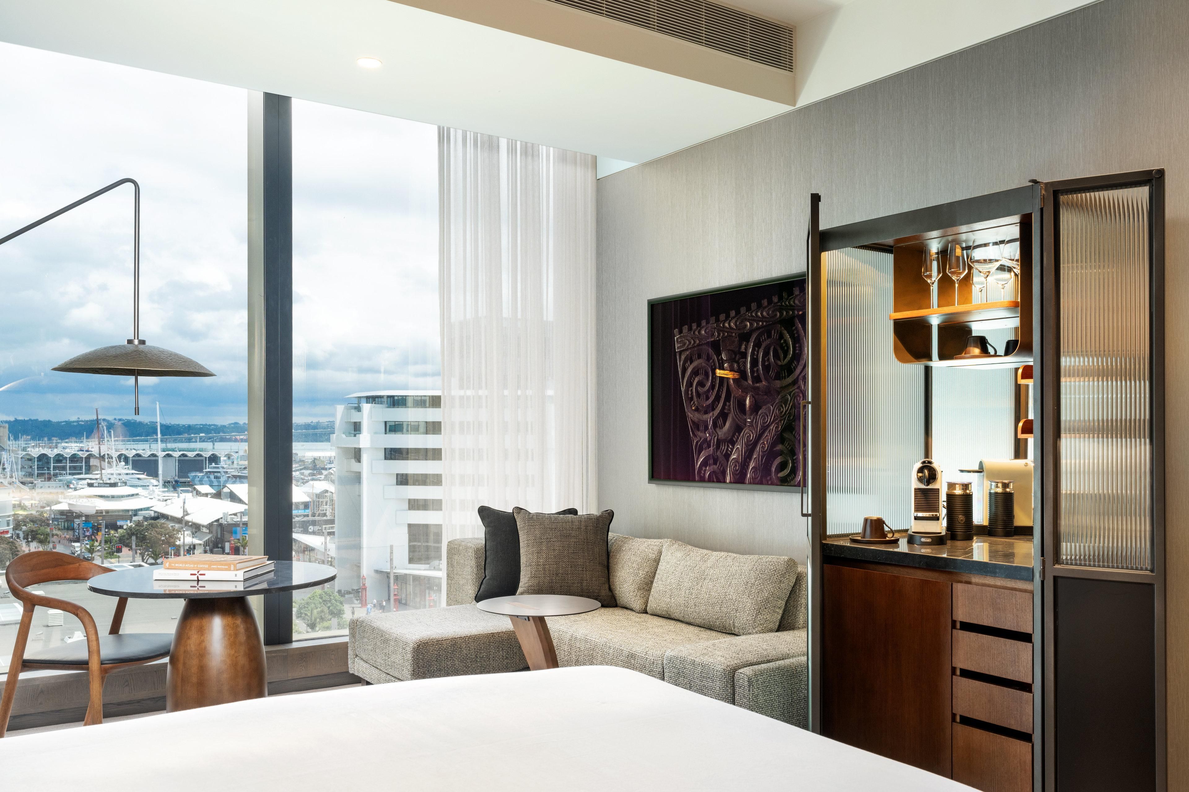 Quarto de hotel moderno com uma janela grande, um sofá, uma mesa pequena e um minibar.