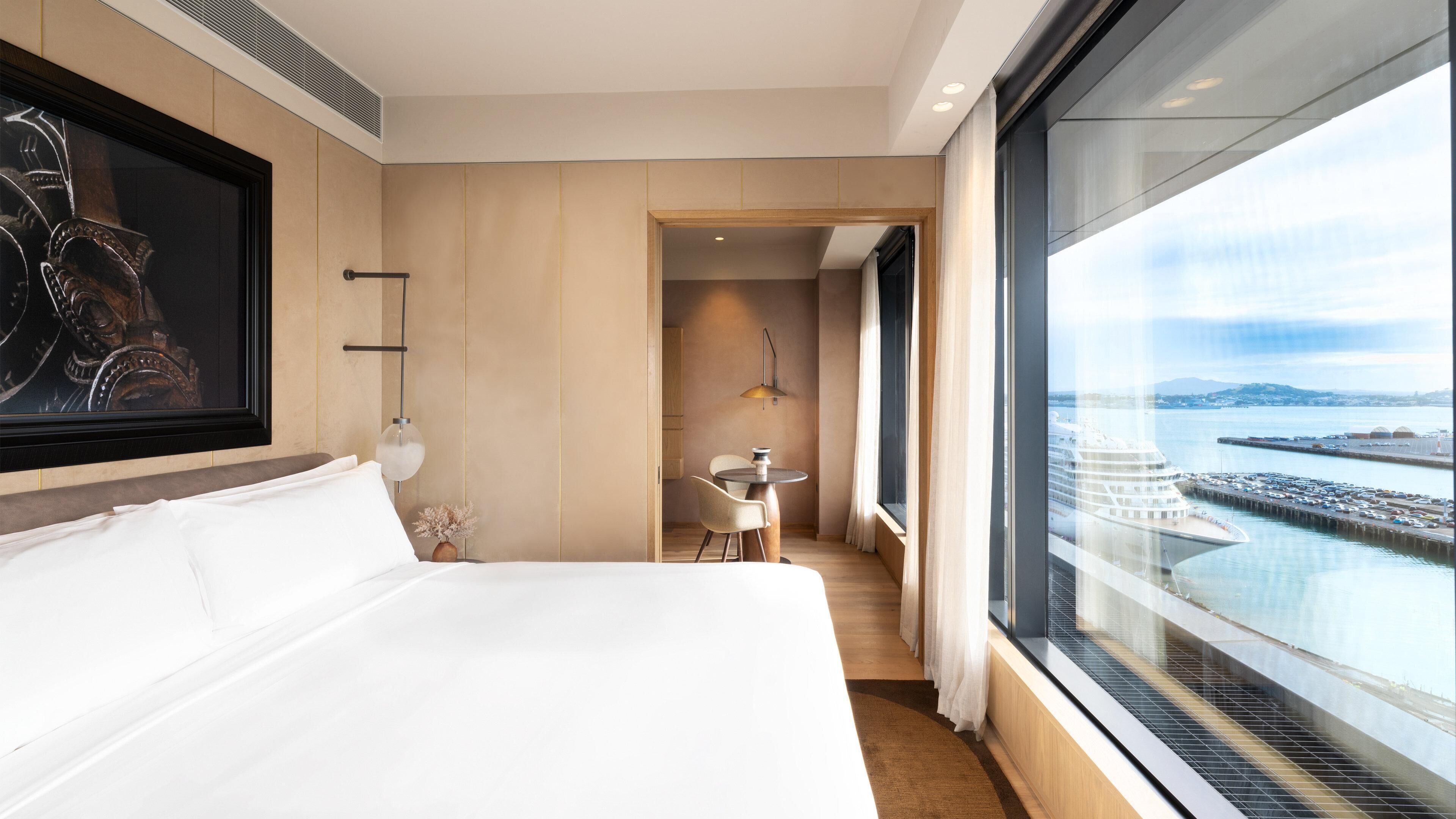 A hotel room with a bed, a desk, and a large window overlooking a body of water.
