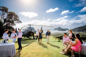 A helicopter parked on a grassy area with a table set for a meal, overlooking a coastal landscape. - Intercontinental Auckland (Auckland)