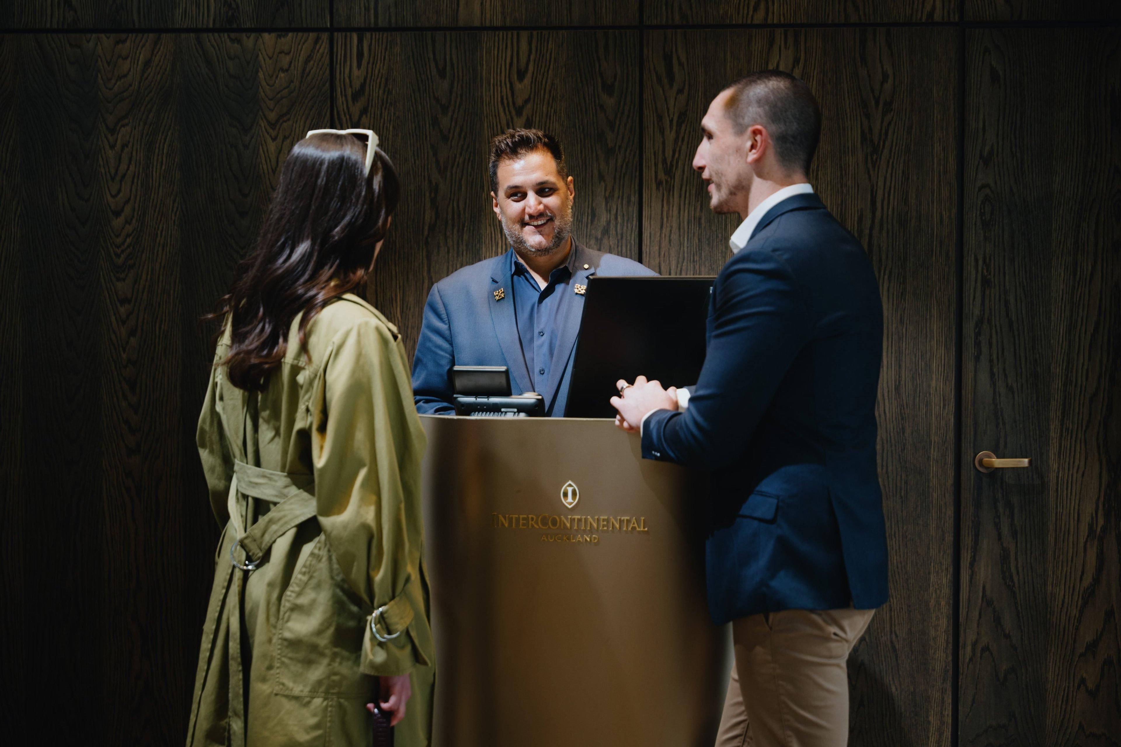 A wooden panel wall, a podium with 'Intercontinental Auckland' branding, and two individuals conversing.