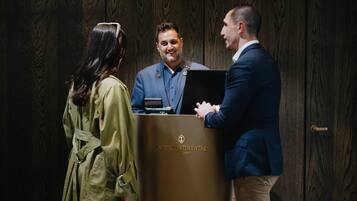 A wooden panel wall, a podium with 'Intercontinental Auckland' branding, and two individuals conversing.