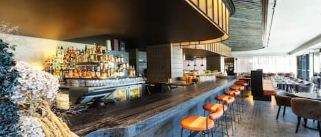 A bar area with a long counter, multiple stools, and a variety of bottles.