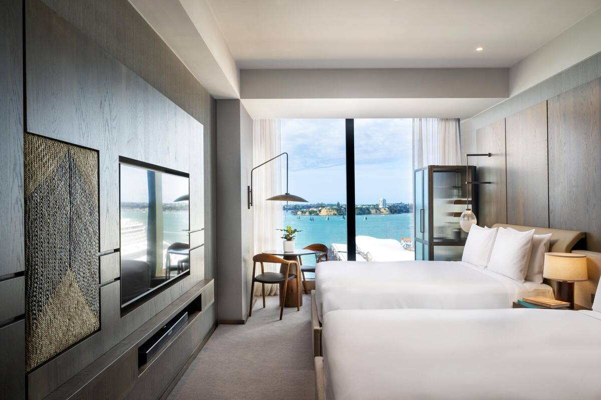 A modern hotel room with a large bed, a TV, a desk, and a view of the sea.