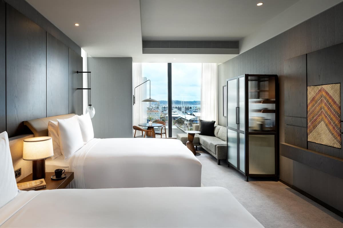 Une chambre d’hôtel moderne avec un grand lit, une table de chevet, une lampe et une vue sur la ville grâce à une grande fenêtre.