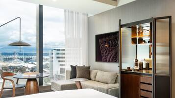 Ein modernes Hotelzimmer mit großem Fenster, einer Couch, einem kleinen Tisch und einer Minibar.