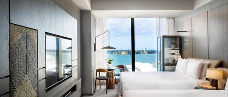 A modern hotel room with a large bed, a TV, a desk, and a view of the sea.