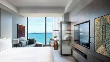 Habitación de hotel moderna con una cama grande, televisor, zona de estar y vistas al mar.