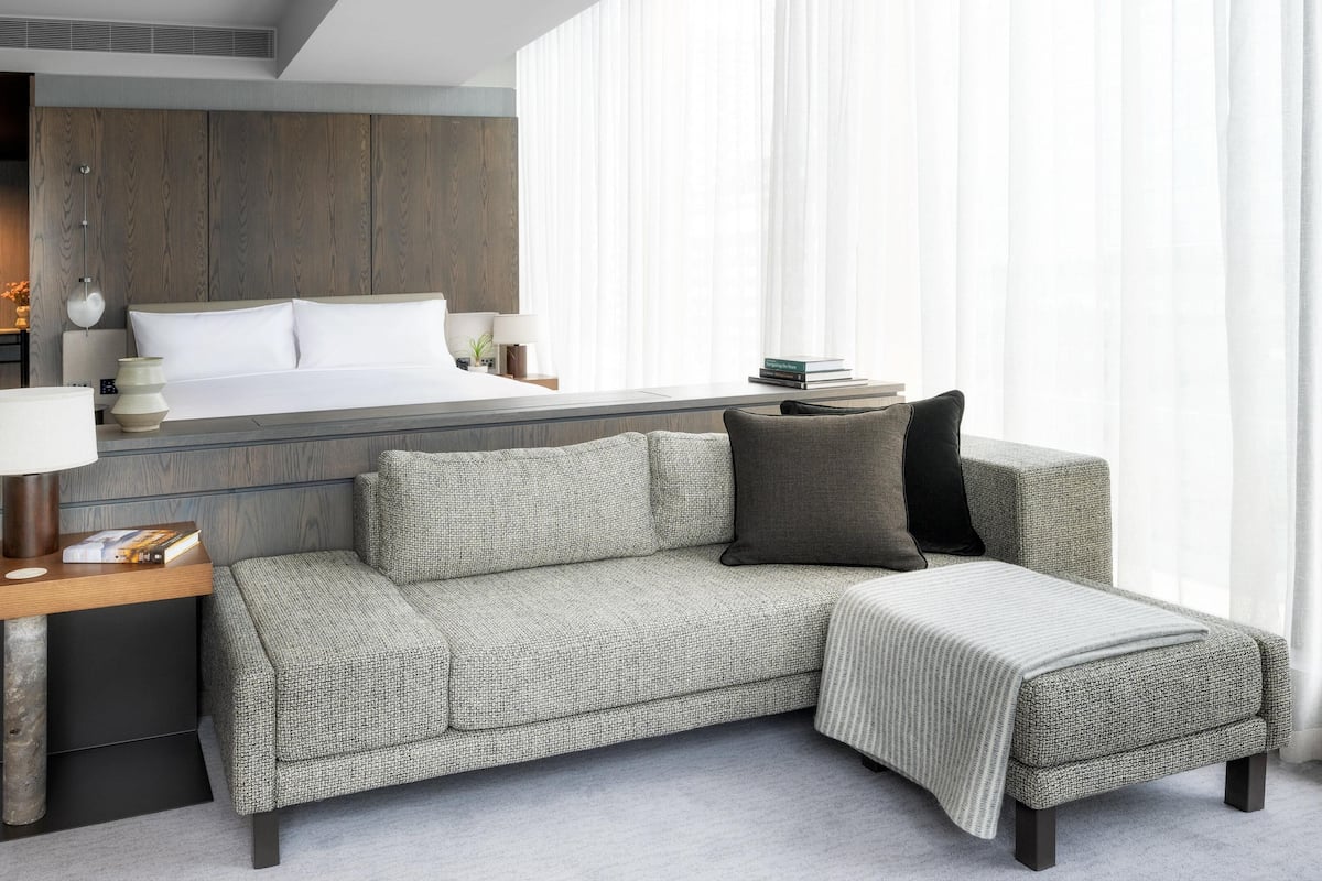 A modern hotel room with a bed, a sofa, a bedside table, and a lamp.