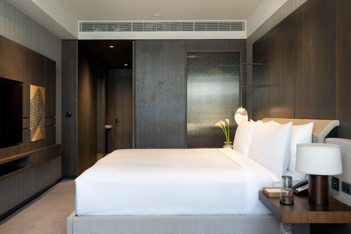 Une chambre d’hôtel moderne avec un grand lit, une télévision, une table de chevet avec une lampe et un panneau décoratif au mur.