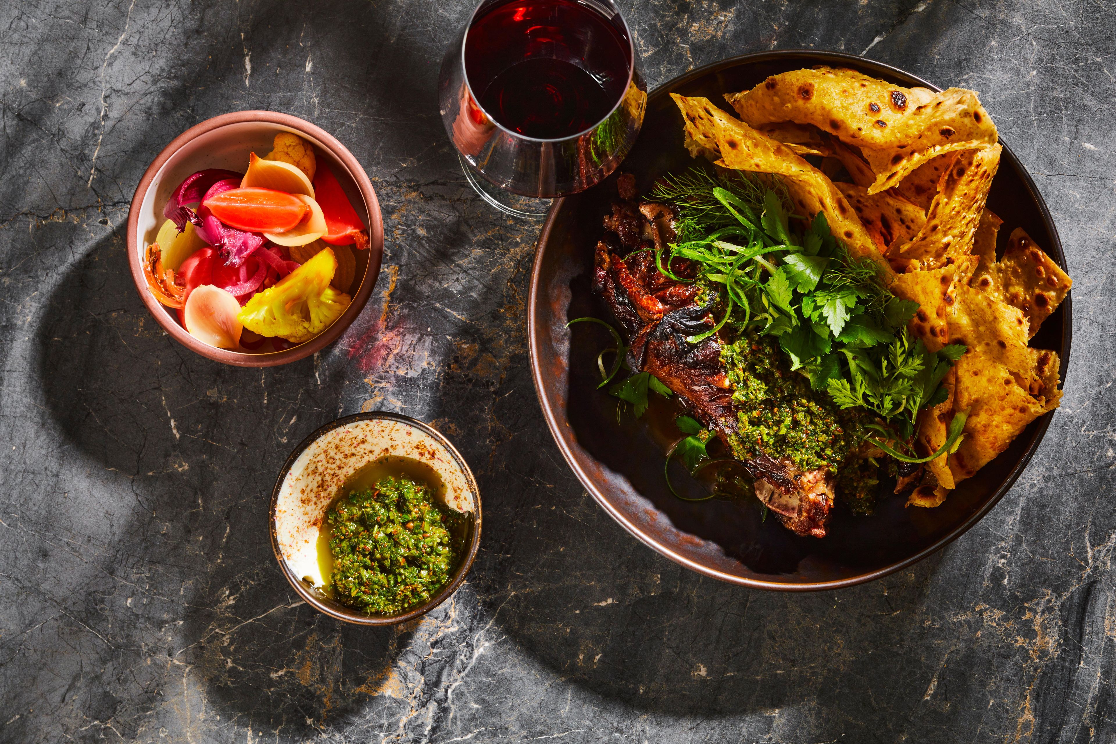 Eine Mahlzeit mit einer Schüssel Gemüse, einem Glas Rotwein und einem Teller Essen auf einer dunklen Oberfläche.
