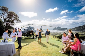 A helicopter parked on a grassy area with a table set for a meal, overlooking a coastal landscape. - Intercontinental Auckland (Auckland)