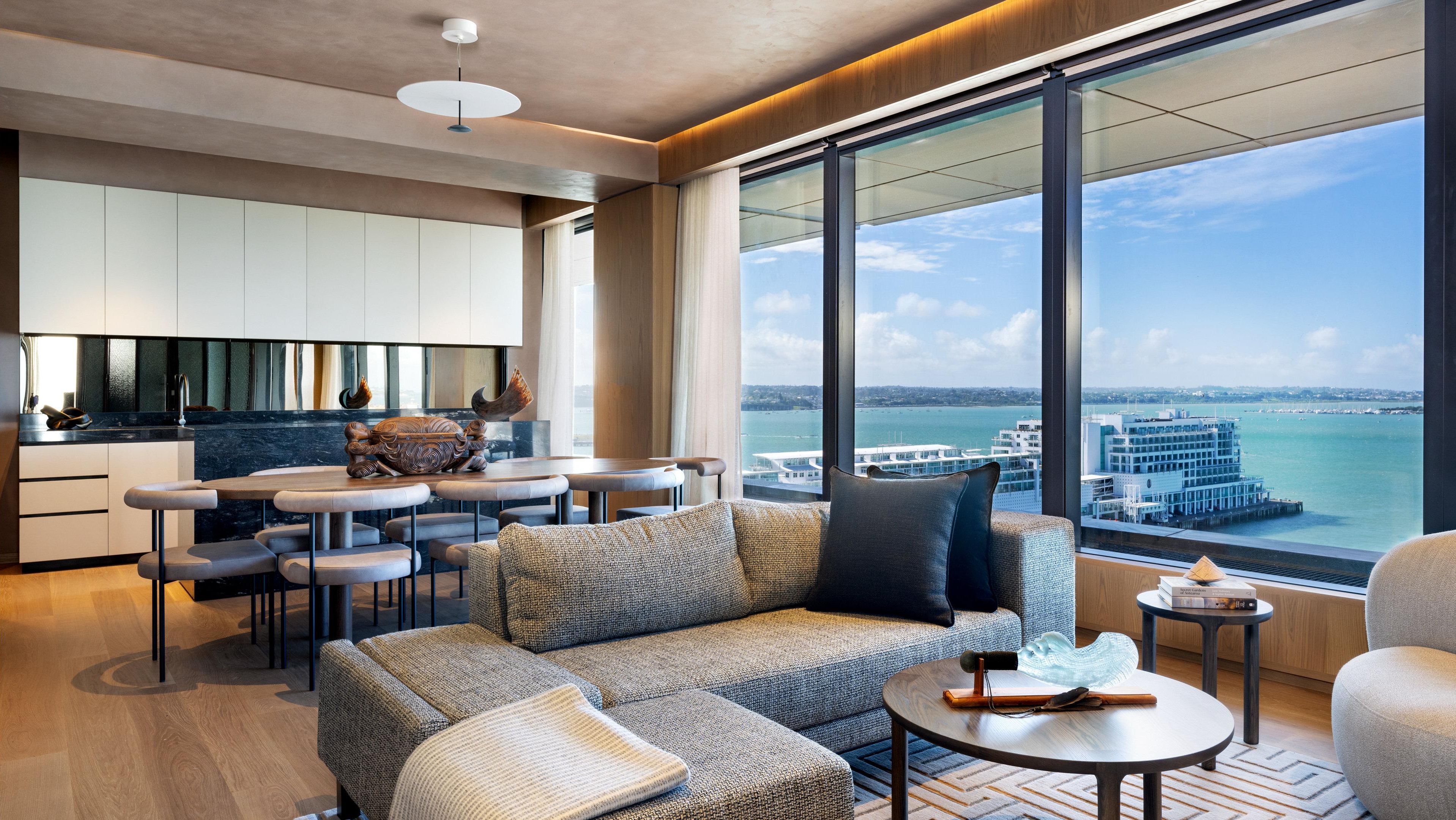 A modern interior with a dining area, sofa, and large windows offering a city and water view.