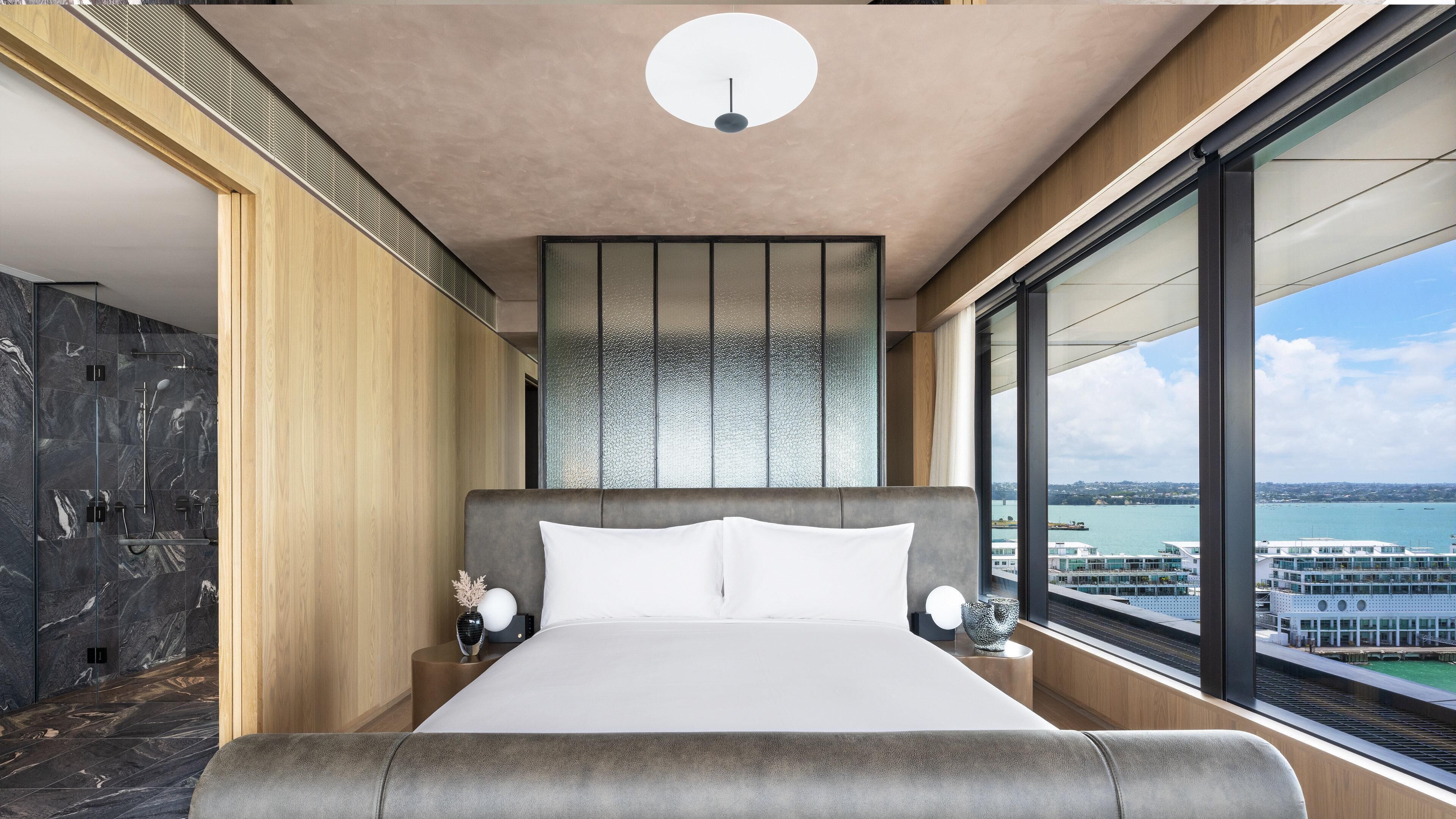 A modern bedroom with a large bed, a view of the water, and a cityscape.