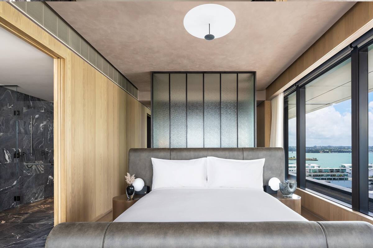 A modern bedroom with a large bed, a view of the water, and a cityscape.