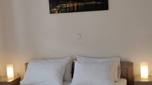 Une chambre à coucher comprenant un lit, deux tables de chevet, une commode, un luminaire suspendu et un tableau encadré accroché au mur.