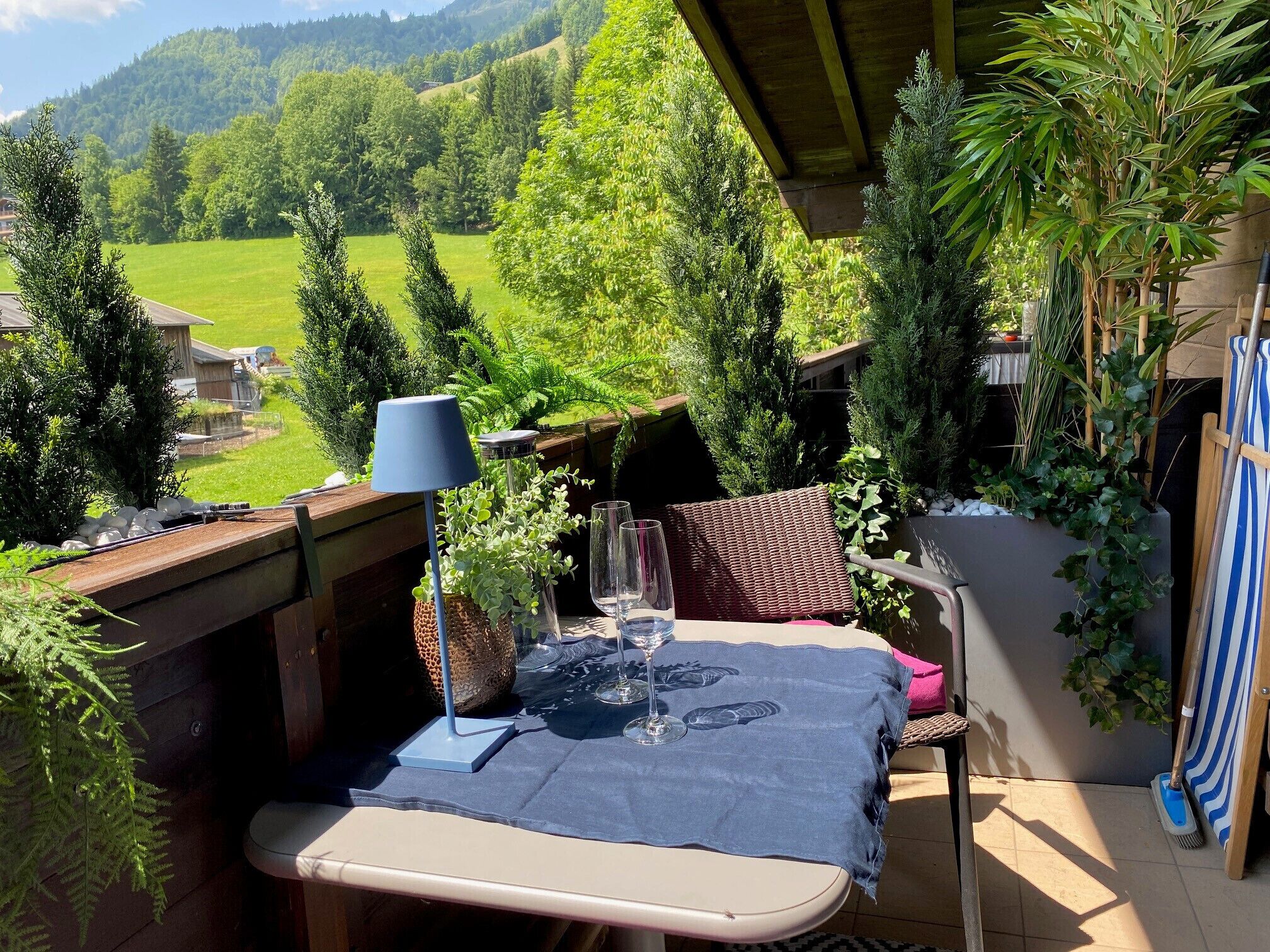 A patio with a table set for two, a lamp, and a view of a green landscape.